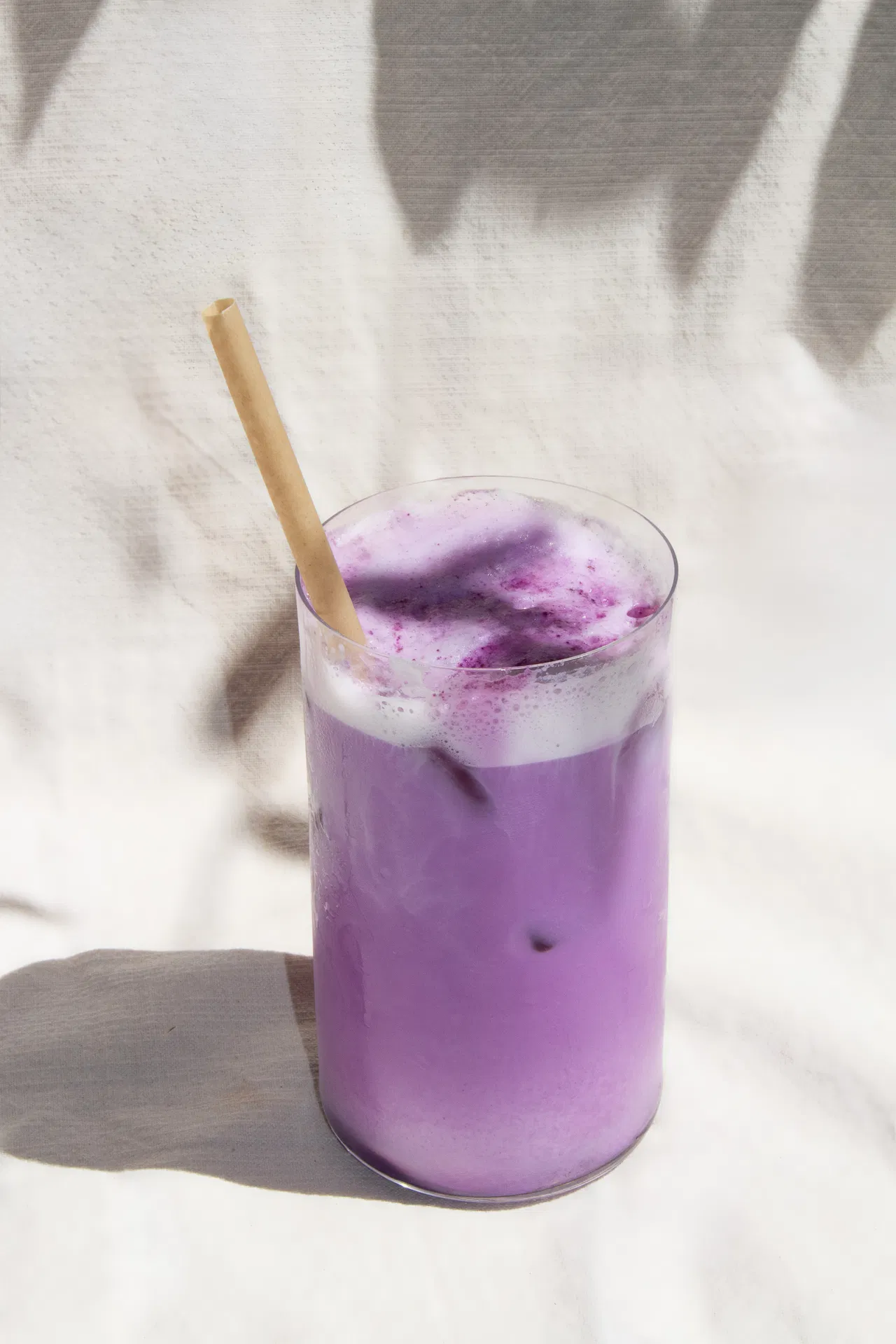 Boisson violette glacée, mousse fine et paille en bambou sur lin clair