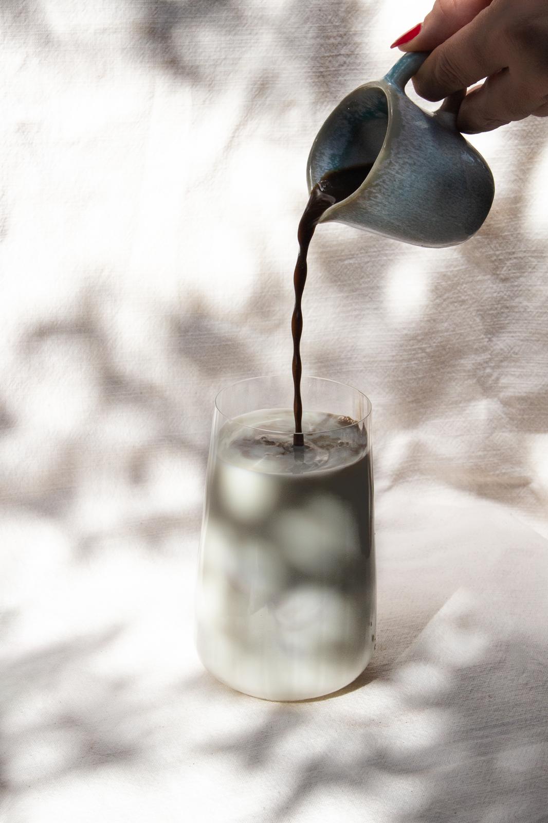 Service d'un café noir dans un verre glacé, lumière douce et ombres portées